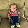 Liam is registered to the contest to win money with this photo: baby, child, infant, plaid_shirt, jeans, socks, couch, furniture, indoor, person, seated, looking_at_camera, cute, young, small, casual_clothing, home, portrait, neutral_expression, living_room