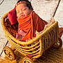 newborn, baby, sleeping, wicker_basket, orange_wrap, headband, cozy, rustic, wooden_floor, carriage, blanket, infant, cute, peaceful, indoors, soft_light, decor, portrait, child, resting