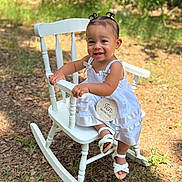 Rachelys is registered to the contest to win money with this photo: baby, child, rocking_chair, white_dress, smiling, outdoor, grass, greenery, hair_buns, sandals, milestone_sign, wooden_sign, happy, portrait, cute, infant, sitting, sunlight, nature, young_child