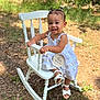 baby, child, rocking_chair, white_dress, smiling, outdoor, grass, greenery, hair_buns, sandals, milestone_sign, wooden_sign, happy, portrait, cute, infant, sitting, sunlight, nature, young_child