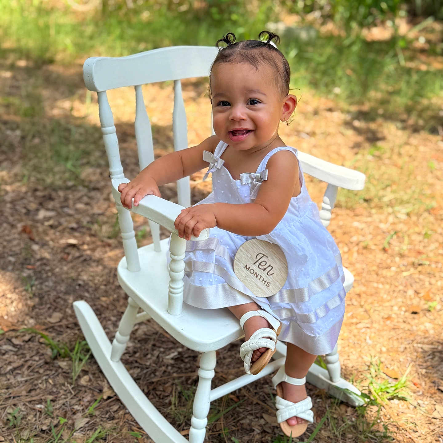 Rachelys is registered to the contest to win money with this photo: baby, child, cute, grass, greenery, hair_buns, happy, infant, milestone_sign, nature, outdoor, portrait, rocking_chair, sandals, sitting, smiling, sunlight, white_dress, wooden_sign, young_child