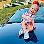 toddler, child, smiling, sitting, car, reflection, shoes, outdoor, grass, house, hair_bow, bracelet, happy, clothing, sidewalk, daylight, nature, portrait, cute, casual