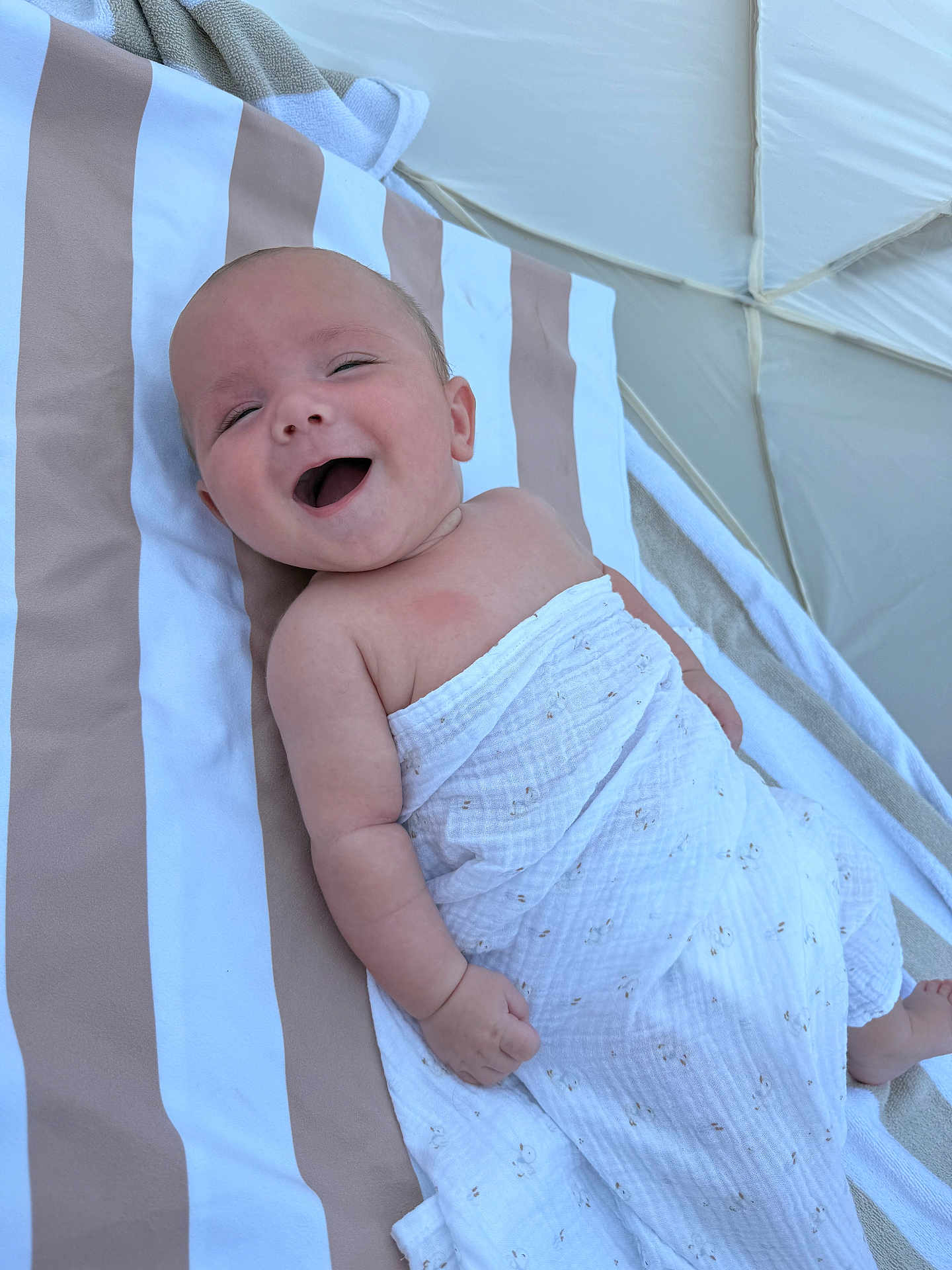 Marin a rejoint le concours — aidez-le/la à gagner de superbes lots ! baby, smiling, blanket, striped_towel, infant, happy, lying_down, skin, arm, hand, face, head, outdoor, natural_light, cute, young_child, portrait, relaxed, white, beige