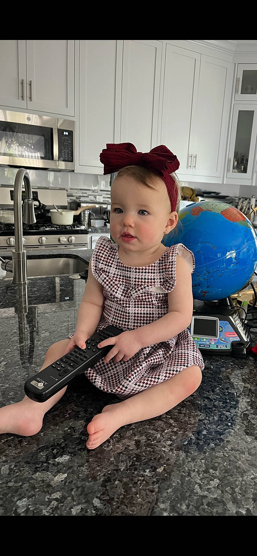 Artemis is registered to the contest to win money with this photo: baby, baby_toddler_clothing, balloon, barefoot, child, countertop, flash_photography, flooring, foot, fun, human_leg, kitchen_appliance, knee, pattern, person, plucked_string_instruments, sandal, sitting, thigh, toddler
