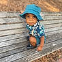 toddler, child, blue_hat, bench, outdoor, curious, sitting, leaf_pattern, shorts, shoes, park, wooden_bench, nature, daylight, cute, portrait, person, casual_clothing, young_child, expression