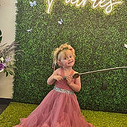 Kinsley is registered to the contest to win money with this photo: child, girl, pink_dress, flower_crown, toy_sword, carpet, green_wall, neon_sign, butterflies, smiling, indoor, playful, costume, dress_up, portrait, cute, happy, floor, decor, person