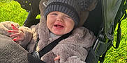 Louie joined the competition — help win amazing prizes! baby, child, smiling, stroller, hat, pom_poms, coat, fuzzy_clothing, outdoor, green_grass, sunlight, happy, infant, seatbelt, baby_stroller, cute, warm_clothing, portrait, young_child, daytime