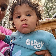Arion is registered to the contest to win money with this photo: toddler, child, curly_hair, blue_outfit, bluey, person, adult_hand, outdoor, trees, wooden_rail, portrait, young_child, casual_clothing, daylight, closeup, expression, holding, face, cute, people