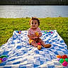 Arion joined the competition — help win amazing prizes! toddler, child, blanket, grass, lake, water, toy, plastic_eggs, outdoor, sunlight, nature, summer, playtime, casual_clothing, shoes, striped_shirt, shorts, curly_hair, sitting, portrait