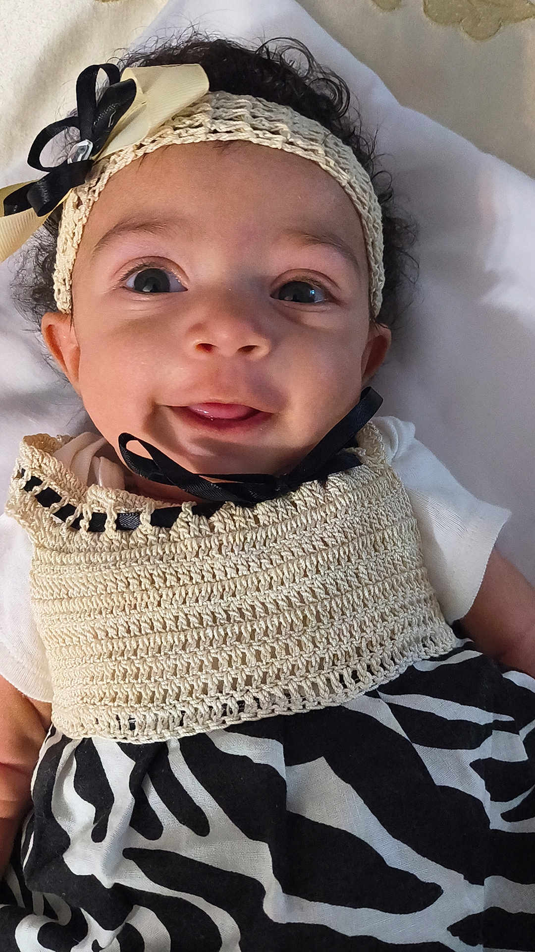 Anastasia joined the competition — help win amazing prizes! baby, infant, child, smile, tongue, headband, bow, curly_hair, eyes, face, cheeks, crochet_top, zebra_print, dress, lying_down, blanket, portrait, close_up, adorable, person