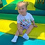 Kiara participe au concours pour gagner de l'argent avec cette photo : toddler, child, inflatable, playground, colorful, yellow, green, blue, socks, tshirt, braids, outdoor, sunlight, play, fun, cute, sitting, person, young_child, smile