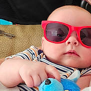 Caspian is registered to the contest to win money with this photo: baby, sunglasses, plush_toy, infant, striped_clothing, hand, face, cute, child, toy, red, blue, soft_toy, comfort, relaxing, indoor, person, portrait, casual, close_up