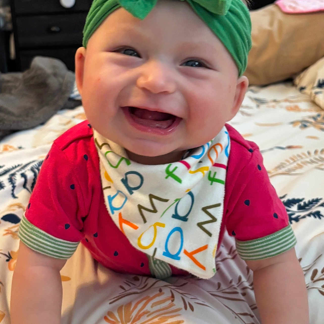 Maaliyah joined the competition — help win amazing prizes! baby, bedspread, bib, bow, child, closeup, colorful, crawling, cute, face, floral_pattern, hands, happy, headband, indoor, infant, person, portrait, red_shirt, smiling