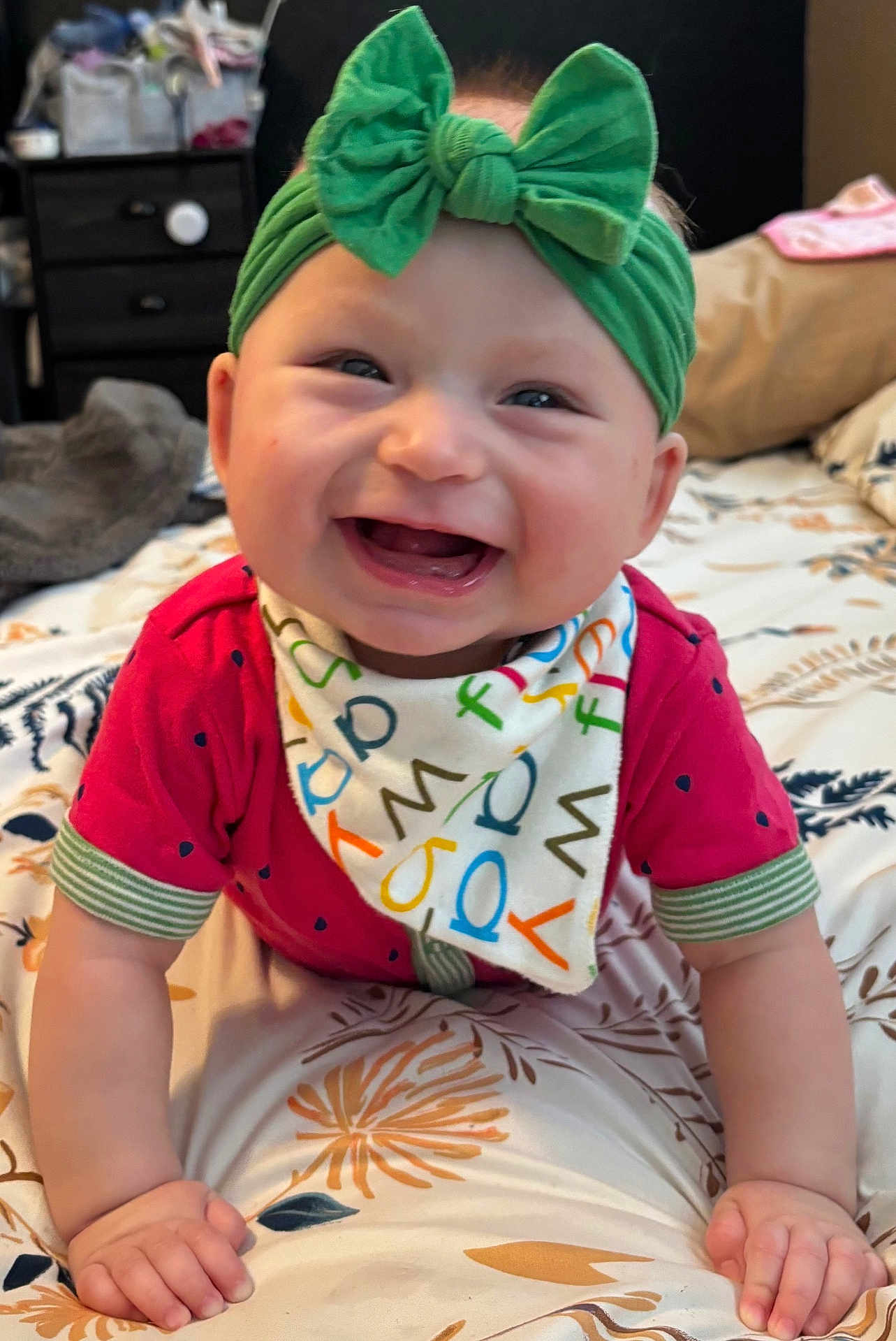 Maaliyah joined the competition — help win amazing prizes! baby, child, smiling, indoor, headband, bow, bib, colorful, red_shirt, hands, bedspread, floral_pattern, happy, cute, person, infant, portrait, closeup, face, crawling