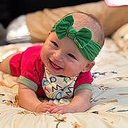 Maaliyah is registered to the contest to win money with this photo: baby, smiling, headband, green_bow, lying_down, blanket, patterned, happy, infant, cute, clothing, toddler, face, portrait, indoors, skin, hands, fun, child, colorful