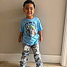 child, boy, smiling, standing, indoor, casual_clothing, blue_tshirt, jeans, curly_hair, shoes, wooden_floor, wall, happy, portrait, fashion, young, cute, person, full_body, colorful
