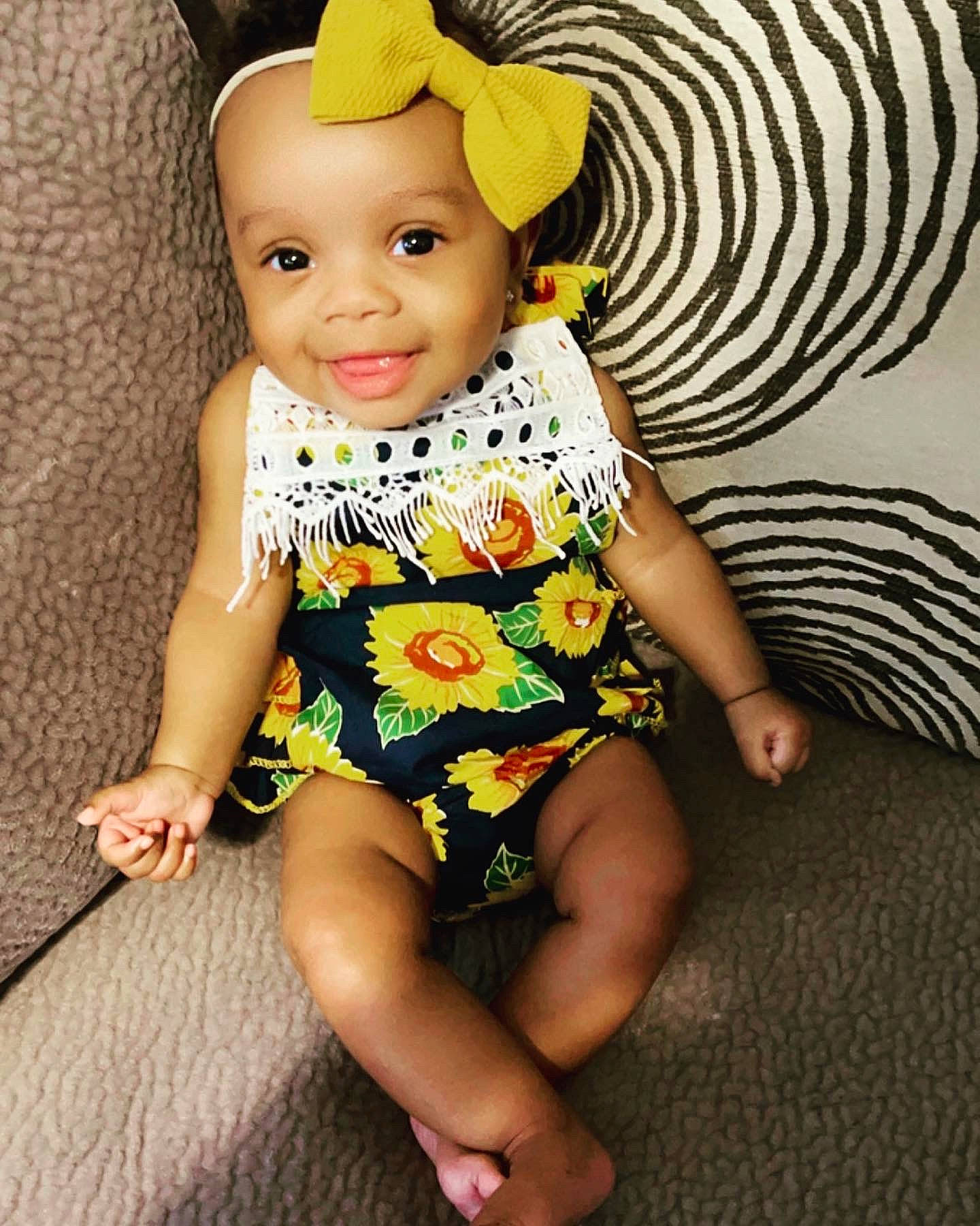 Indi is registered to the contest to win money with this photo: baby, baby_laughing, baby_products, baby_toddler_clothing, barefoot, child, costume_accessory, day_dress, finger, foot, headband, headwear, joy, mouth, nose, one_piece_garment, person, pillow, skin, throw_pillow