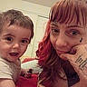 child, woman, tattoos, bed, indoor, person, face, smile, curly_hair, red_hair, short_hair, expression, casual_clothing, hand, portrait, closeup, happy, toddler, interaction, home