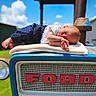 baby, sleeping, blanket, tractor, ford, blue, outdoor, sunny, sky, clouds, infant, clothing, white_shirt, pants, peaceful, resting, vintage, vehicle, farm, cute