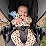 baby, stroller, plush_toy, onesie, leopard_print, infant, outdoor, grass, pavement, happy, smiling, face, hand, foot, safety_belt, child, cute, person, toy, seat