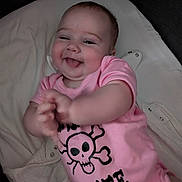 Ellie is registered to the contest to win money with this photo: apparel, baby, baby_clothes, blanket, child, clapping_hands, closeup, cute, face, happy, indoor, infant, lying_down, person, pink_onesie, pirate, portrait, skull_design, smiling, soft_lighting