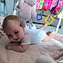 baby, infant, blanket, plush_toy, stuffed_animal, colorful_toys, floor_play, nursery, child, cute, soft_texture, indoors, playtime, smiling, clothing, white_onesie, carpet, furniture, happy, young_child