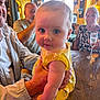 Ellie joined the competition — help win amazing prizes! baby, child, adult, hand, yellow_clothing, table, glass, drink, indoor, people, face, portrait, seated, curious, holding, cozy, warm_lighting, rustic, restaurant, family