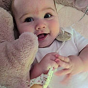 Ellie joined the competition — help win amazing prizes! baby, smiling, face, toy, teddy_bear, hand, blanket, infant, cute, child, white_clothing, pacifier_clip, soft_texture, lying_down, happy, closeup, indoors, comfort, playful, young