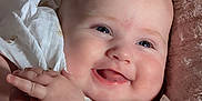 Ellie is registered to the contest to win money with this photo: baby, blanket, blue_eyes, cheeks, closeup, clothing, cuddly, cute, face, hands, happy, indoors, infant, joyful, portrait, skin, smiling, soft, white_dress, young_child