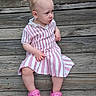 toddler, child, pink_crocs, striped_dress, wooden_steps, outdoor, sitting, curious_expression, pony_tail, footwear, person, casual_clothing, summer, daylight, young_child, portrait, wood_texture, planks, candid, cute