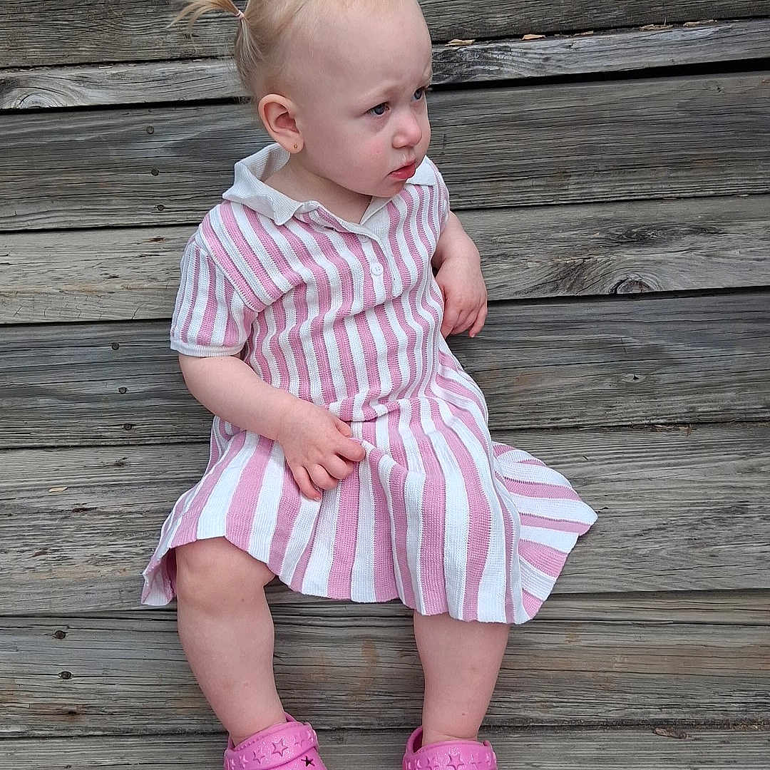 Fiona joined the competition — help win amazing prizes! toddler, child, pink_crocs, striped_dress, wooden_steps, outdoor, sitting, curious_expression, pony_tail, footwear, person, casual_clothing, summer, daylight, young_child, portrait, wood_texture, planks, candid, cute