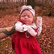 Lilah Jean joined the competition — help win amazing prizes! baby, infant, child, headband, red_dress, long_sleeve, patterned_clothing, puckered_face, closed_eyes, arm, tattoo, hand, outdoors, forest, fallen_leaves, autumn, tree, portrait, person_holding, cute_expression