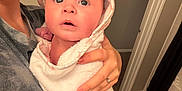 Lilah Jean is registered to the contest to win money with this photo: baby, infant, hooded_towel, towel_wrap, surprised_expression, adult_hand, engagement_ring, manicured_nails, parent, bathroom, mirror, polaroid_photos, framed_art, leopard_rug, tile_floor, bathmat, closeup, portrait, holding, doorway