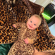 Lilah Jean is registered to the contest to win money with this photo: baby, dog, leopard_print, blanket, onesie, smile, indoor, pet, cute, child, animal, sleepwear, furniture, cozy, happy, face, person, comfort, pattern, home