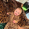 animal, baby, blanket, child, comfort, cozy, cute, dog, face, furniture, happy, home, indoor, leopard_print, onesie, pattern, person, pet, sleepwear, smile