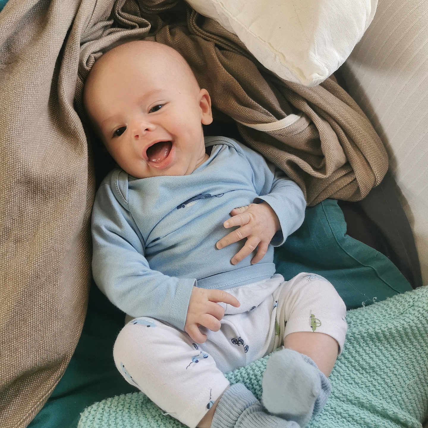 Noah participe au concours pour gagner de l'argent avec cette photo : baby, blanket, blue_clothing, child, comfortable, cozy, cute, happy, indoor, infant, knitted, pillow, portrait, resting, sitting, sleepwear, small_hands, smiling, soft_texture, warm