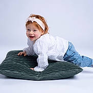 Inaya a rejoint le concours — aidez-le/la à gagner de superbes lots ! toddler, child, headband, red_hair, white_shirt, blue_jeans, cushion, smiling, playful, barefoot, studio, portrait, happy, crawling, indoors, cute, young_child, fashion, casual_wear, white_background