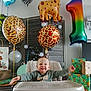 baby, balloons, celebration, cheerful, child, gifts, giraffe_balloon, happy, highchair, indoor, leopard_print_balloon, number_one_balloon, onesie, party_decor, present_stack, smile, toddler, tray, wooden_panels, wrapped_presents