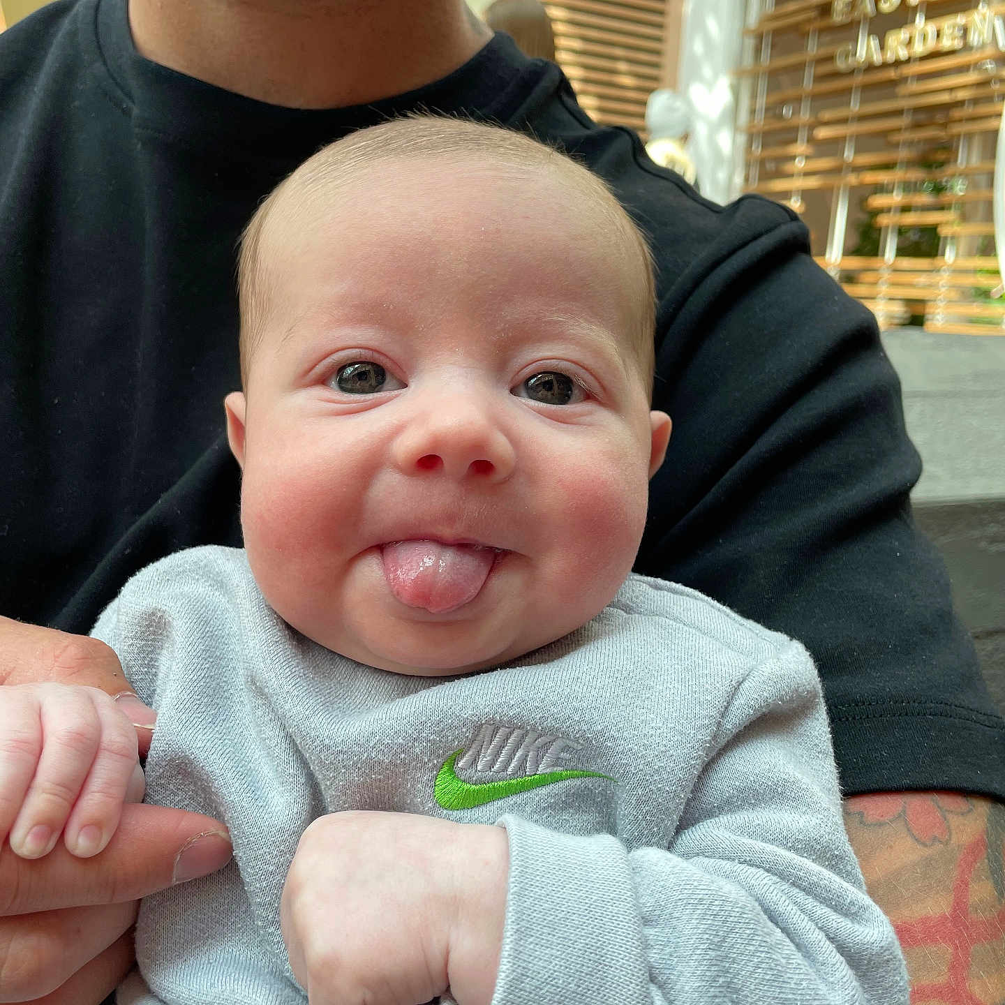 Presley is registered to the contest to win money with this photo: adult, baby, beard, casual_clothing, child, closeup, cute, face, hand, holding, indoor, light, nike, person, playful, smile, sweatshirt, tattoo, tongue, window