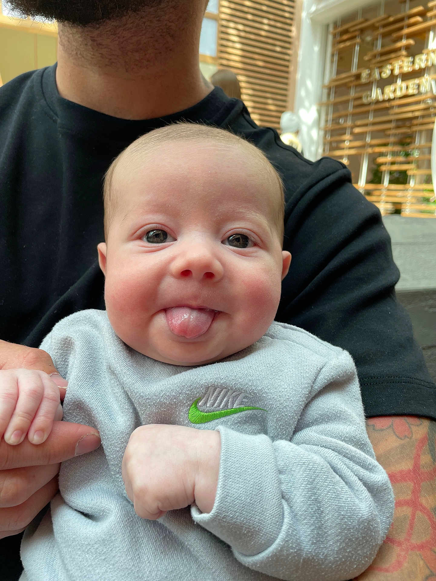 Presley is registered to the contest to win money with this photo: baby, child, tongue, smile, face, person, hand, holding, tattoo, sweatshirt, nike, adult, beard, indoor, window, light, casual_clothing, closeup, cute, playful