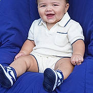 Kamarri is registered to the contest to win money with this photo: baby, smiling, child, knitted_clothing, white_outfit, blue_shoes, sneakers, cushion, chair, drool, happy, portrait, cute, sitting, outdoor, infant, person, fashion, casual, comfortable