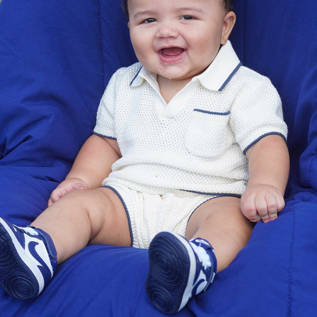 Kamarri is registered to the contest to win money with this photo: baby, smiling, child, knitted_clothing, white_outfit, blue_shoes, sneakers, cushion, chair, drool, happy, portrait, cute, sitting, outdoor, infant, person, fashion, casual, comfortable