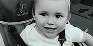 Thiago participe au concours pour gagner de l'argent avec cette photo : toddler, child, smile, face, stroller, seatbelt, indoors, black_and_white, happy, baby, person, hair, clothing, sitting, seat, straps, toy, expression, young_child, portrait