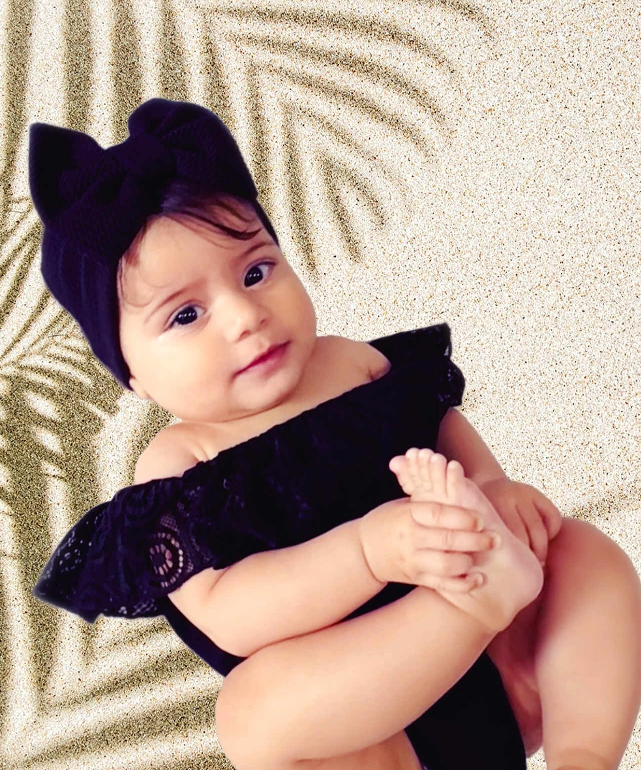 Milenna is registered to the contest to win money with this photo: baby, child, black_clothing, headband, foot, hand, skin, portrait, cute, infant, toddler, smile, playful, sitting, closeup, person, indoors, soft_light, background, fashion