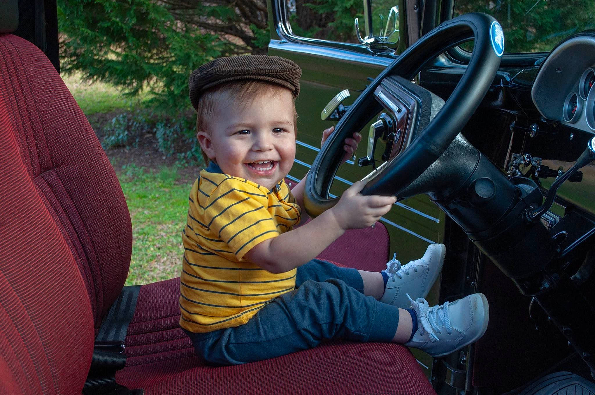 Maddox is registered to the contest to win money with this photo: auto_part, car, child, family_car, joy, motor_vehicle, person, plant, smile, steering_part, steering_wheel, toddler, vacation, vehicle