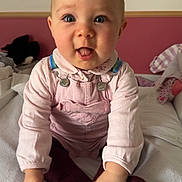 Eléonore participe au concours pour gagner de l'argent avec cette photo : baby, infant, child, pink_clothing, overalls, sitting, blanket, indoor, face, hands, playful, cute, soft_toys, expression, person, head, tongue_out, bright_eyes, cozy_room, casual