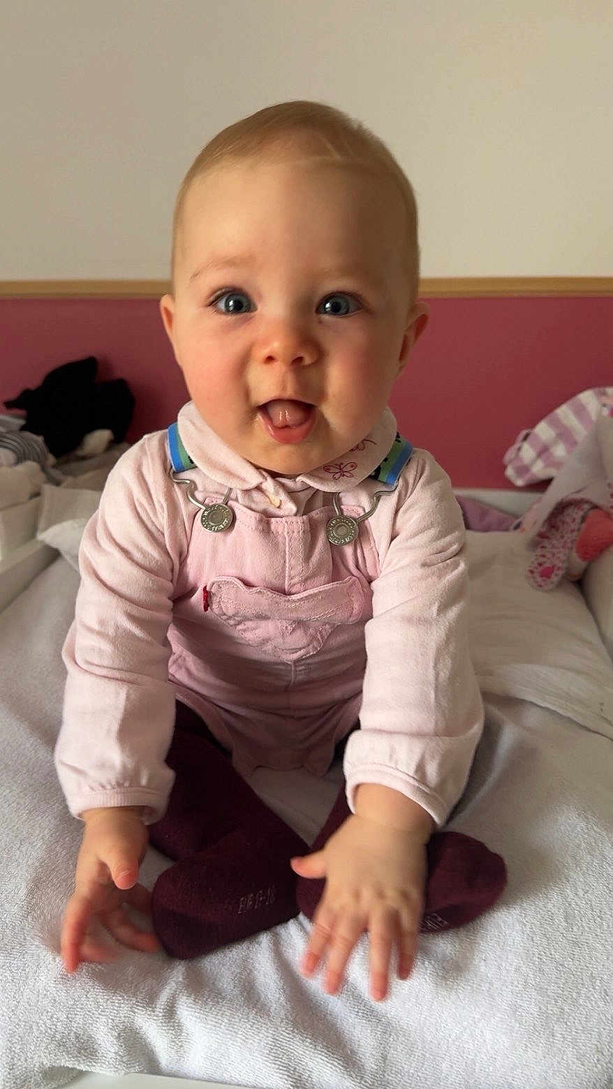 Eléonore participe au concours pour gagner de l'argent avec cette photo : baby, infant, child, pink_clothing, overalls, sitting, blanket, indoor, face, hands, playful, cute, soft_toys, expression, person, head, tongue_out, bright_eyes, cozy_room, casual