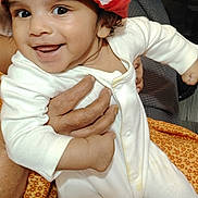 Liam joined the competition — help win amazing prizes! baby, child, smiling, santa_hat, white_onesie, infant, happy, portrait, hand, adult, holding, cozy, indoors, blanket, pattern, cute, festive, holiday, face, person