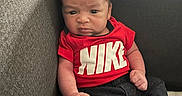 Mateo is registered to the contest to win money with this photo: baby, infant, child, red_shirt, nike_logo, jeans, blue_socks, sofa, couch, indoor, furniture, person, portrait, expression, serious, small_hands, cute, sitting, home, young