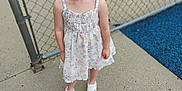 Hermonie is registered to the contest to win money with this photo: child, girl, smiling, pigtails, blonde_hair, blue_eyes, dress, floral_pattern, sneakers, pink_hearts, chain_link_fence, playground, concrete, outdoor, happy, person, young_child, standing, casual_clothing, daylight